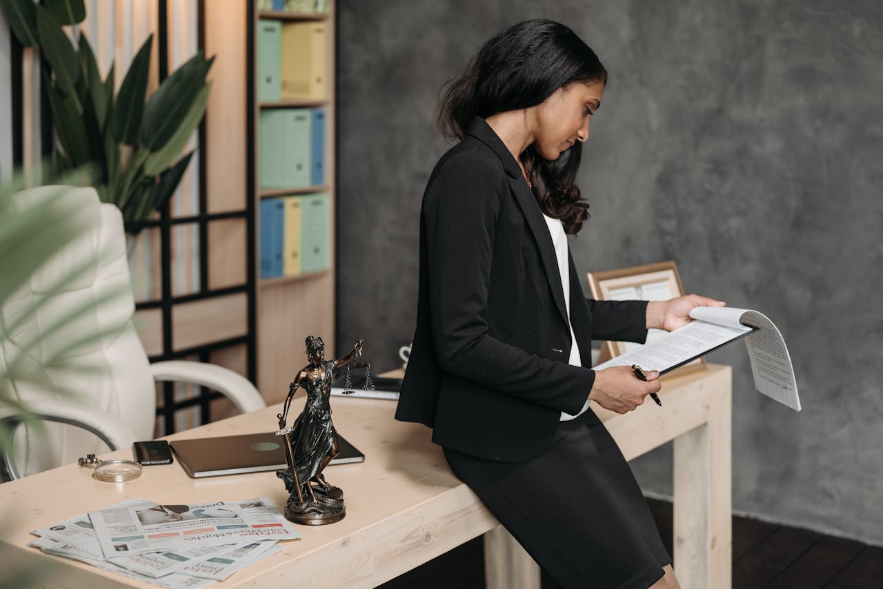 services-02 A professional woman in a business suit reviews legal documents at her office desk.